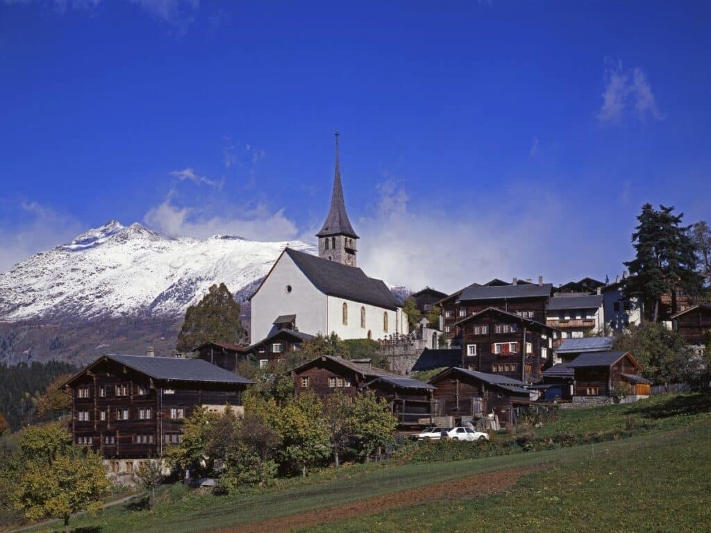 Ernen im Wallis: Holzhäuser und Kirche vor verschneiten Bergen